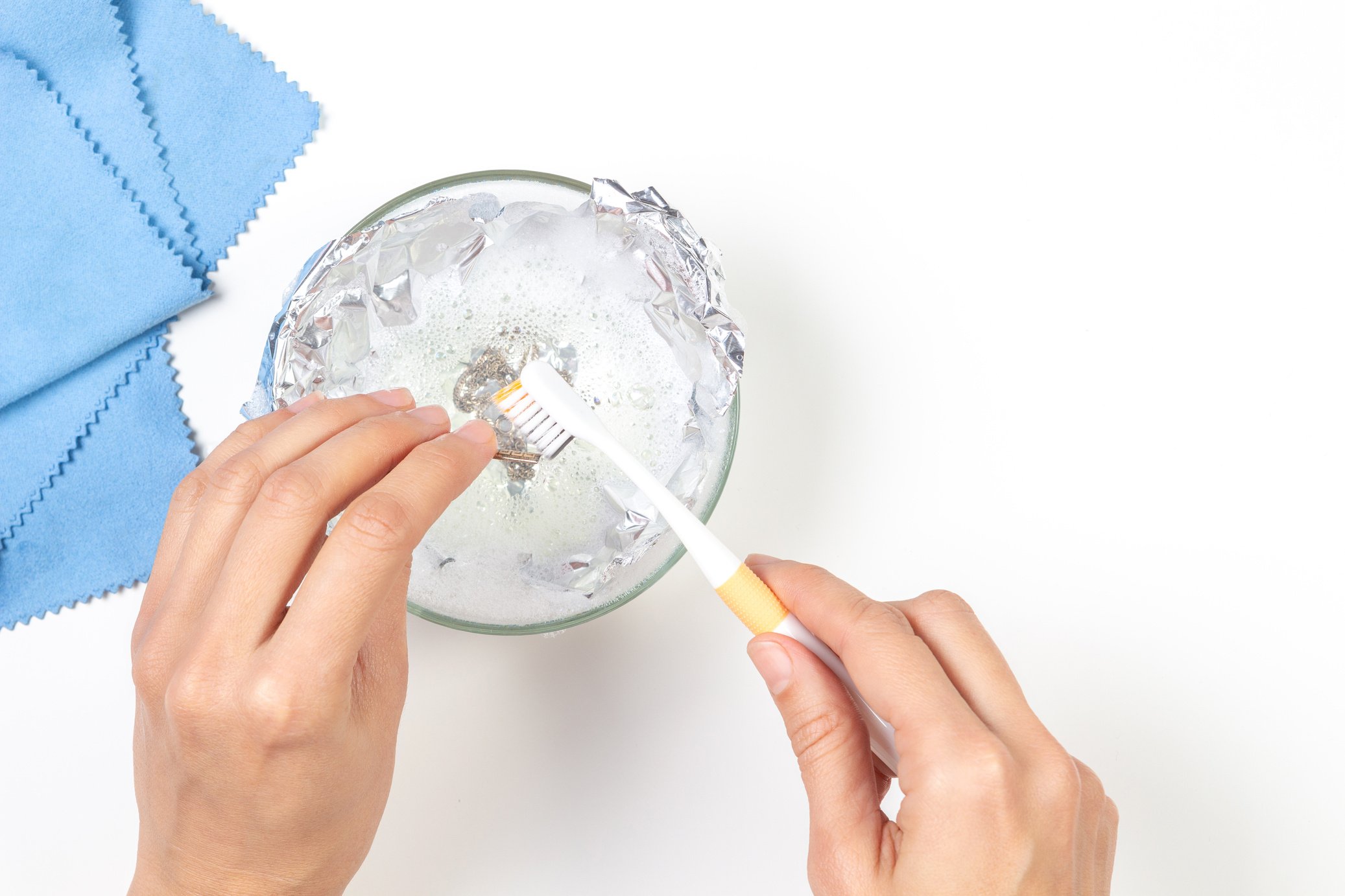 Woman hands cleaning silver jewelry at home. Top view